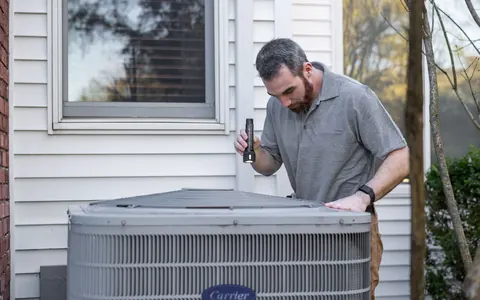 A technician inspecting a residential outdoor HVAC unit — illustrative photo, not City Heating & Cooling